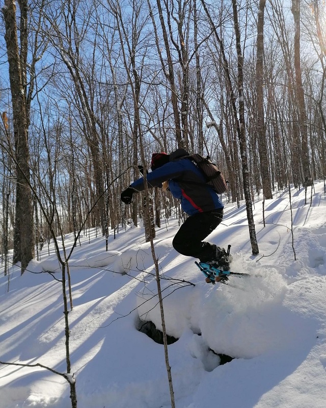 Une personne avec des raquettes aux pieds qui saute dans la neige