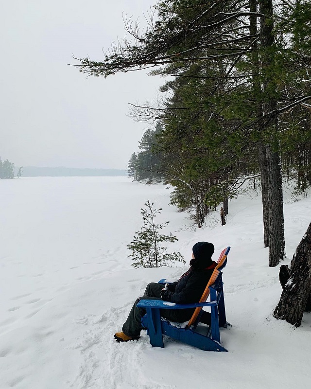 Une personne assise sur une chaise en bois qui contemple le lac gelé