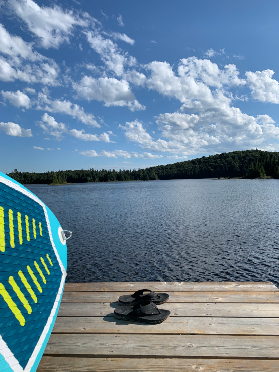 Vue du lac depuis le ponton, planche de paddle bleue et tongs au premier plan